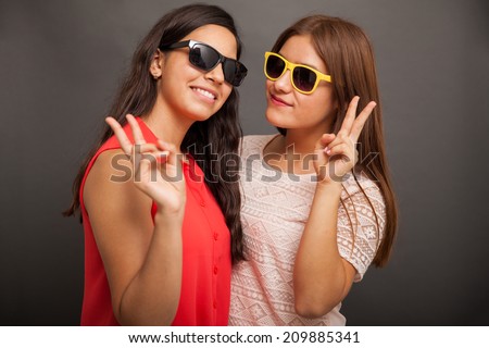 Portrait a couple of teenage girlfriends wearing sunglasses and doing a peace sign with their hands
