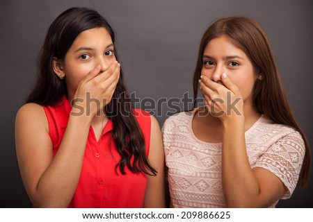 Couple of teen friends covering their mouths as a sign of surprise from the latest gossip
