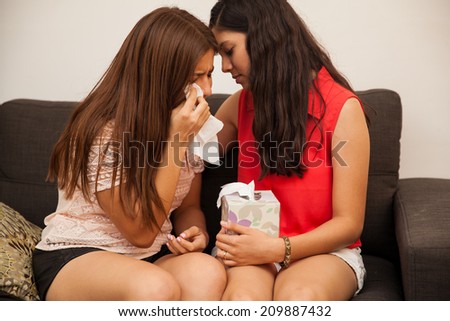 Hispanic teenager comforting her sad and crying friend at home