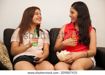Cute female teens hanging out at home while eating snacks and drinking soda