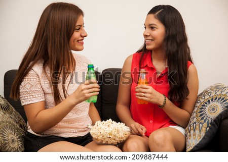 Cute couple of teenage girlfriends drinking soda and eating popcorn before watching a movie