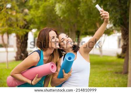 Cute female friends taking a selfie with their smart phone while doing yoga at a park