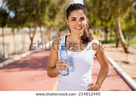 Beautiful young runner holding a bottle of water at a running track