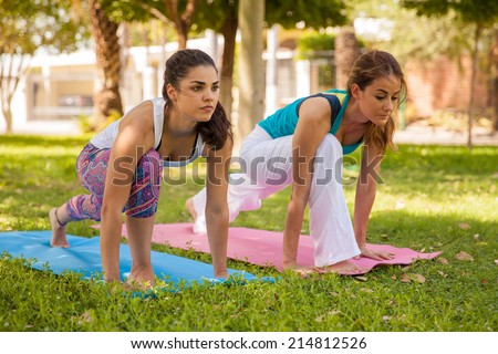 Beautiful female friends trying the high lung yoga pose at a park