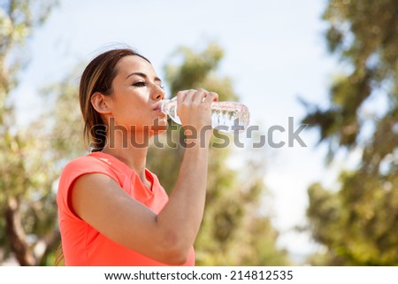 Young Hispanic woman drinking water from a bottle and cooling off after her workout