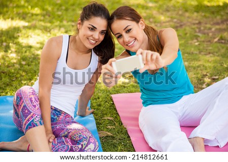 Cute girls taking a selfie with their phone while they do some yoga at a park