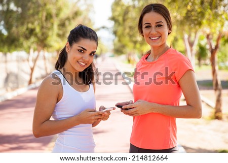Cute young women social networking on their mobile phones before going for a run at a track