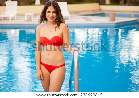 Cute young woman wearing a bikini standing by a pool and smiling
