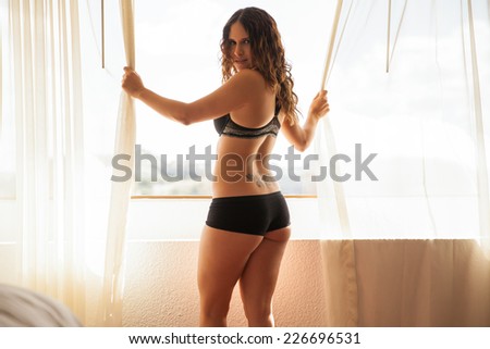 Pretty young woman in underwear looking outside her window at a hotel room