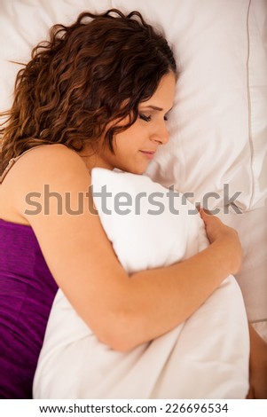 Beautiful brunette with curly hair sleeping on her bed and hugging a pillow
