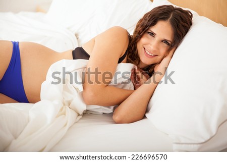 Happy young woman in underwear sleeping in her bed and covering herself with the bed sheets