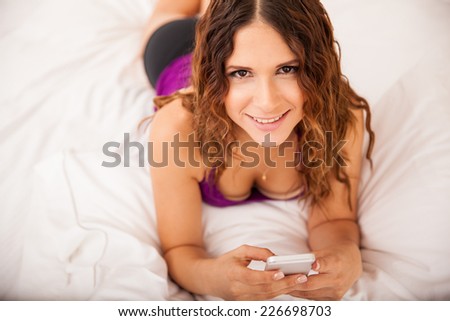 Beautiful young woman social networking with her cell phone while relaxing in bed