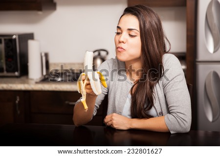 Healthy young woman eating a banana while sitting in the kitchen