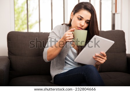 Gorgeous brunette taking a sip of coffee while doing some social networking at home