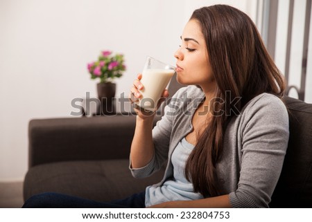 Profile view of a young brunette taking a sip from a glass of milk in the living room