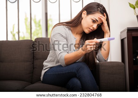 Cute worried girl sitting on a couch at home while reading the results of her recent pregnancy test