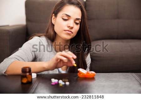 Beautiful young woman using a pill organizer to sort some of her vitamins out at home