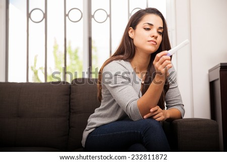 Beautiful young woman reading a pregnancy test while sitting in a couch at home