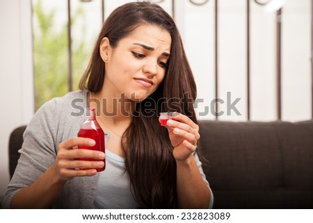 Young brunette disgusted of some cough syrup she has to drink to feel better