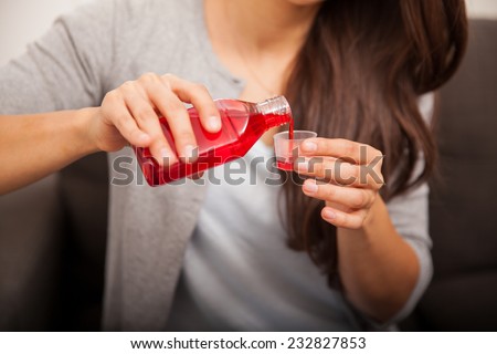 Closeup of a young woman pouring some red cough syrup in a bottle cap