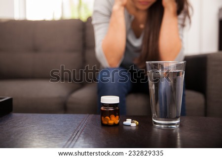 Closeup of a glass of water sitting next to some medicine with a young woman in the background