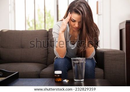Young Latin woman having a bad headache and taking some aspirin to feel better