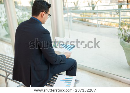 Young businessman sitting on a bench while looking at some performance charts at work