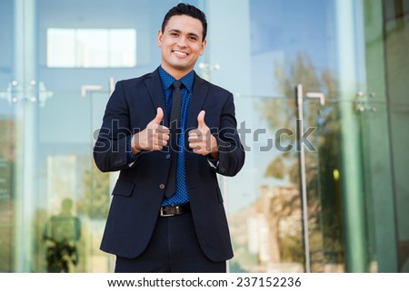 Good-looking Latin young man wearing a suit and giving both thumbs up while smiling excitedly