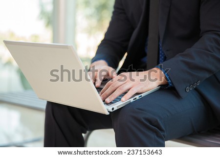 Closeup of a businessman working on a laptop computer while sitting on a bench