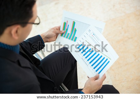 Point of view of a businessman looking at a couple of charts and reviewing performance