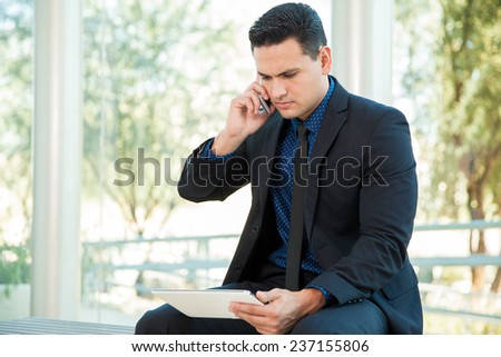 Handsome young businessman talking over the phone with his cell phone while using a tablet computer
