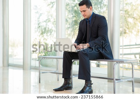 Good-looking young businessman working on a laptop computer while sitting on a bench