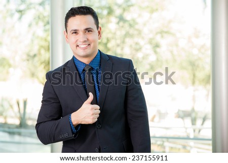 Young Hispanic man wearing a suit and giving his approval with a thumb up