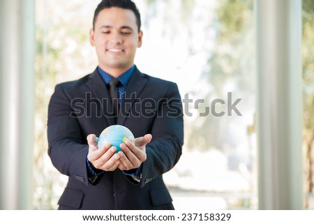 Young Latin businessman holding a small globe in his hands and smiling. Focus on the globe