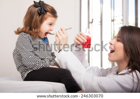 Pretty pediatrician giving some cough syrup to a little girl in her office