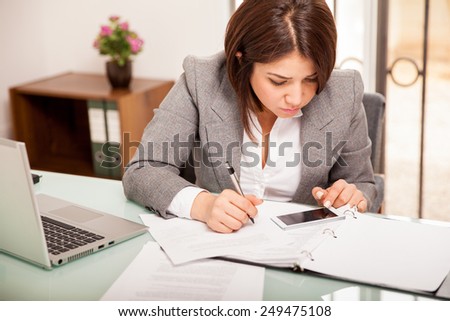 Pretty young business woman using her smart phone to work on her taxes at an office