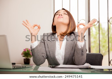 Stressed young business woman doing some breathing exercises and meditating at her office