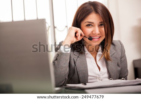 Pretty Latin sales representative wearing a headset and smiling at her office