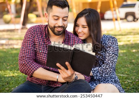 Cute Hispanic couple enjoying a good read together while relaxing outdoors