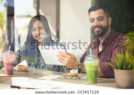 Pretty young Latin couple using a tablet computer at a cafe while eating lunch