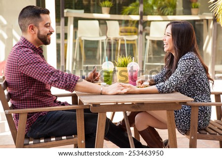 Profile view of a young couple holding hands during a lunch date and having fun