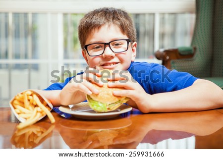 Happy blond tween enjoying a hamburger and french fries at home