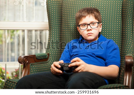 Little boy with glasses relaxing and playing video games at home