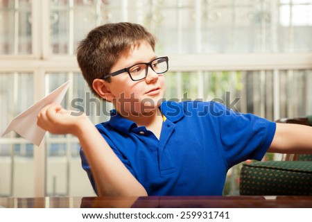 Cute blond kid with glasses playing at home with a paper plane