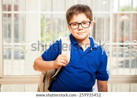 Portrait of a cute young boy with glasses carrying a backpack and standing ready for school