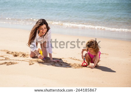 Happy young single mother having fun with her daughter and drawing together in the sand