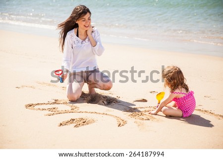 Young Hispanic mother and her little daughter drawing in the sand on a sunny day