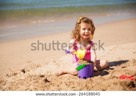 Portrait of a little white girl playing with buckets of sand at the beach and smiling