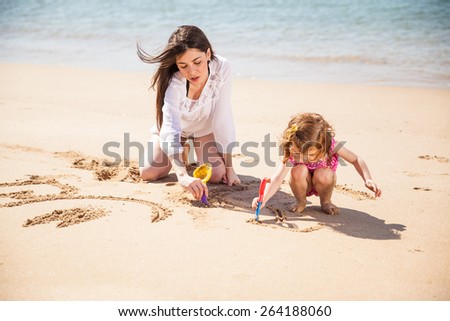 Portrait of a young mother and her daughter enjoying a sunny day at the beach and drawing in the sand