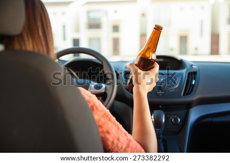 Rear view of a young brunette holding a bottle of beer while driving a car